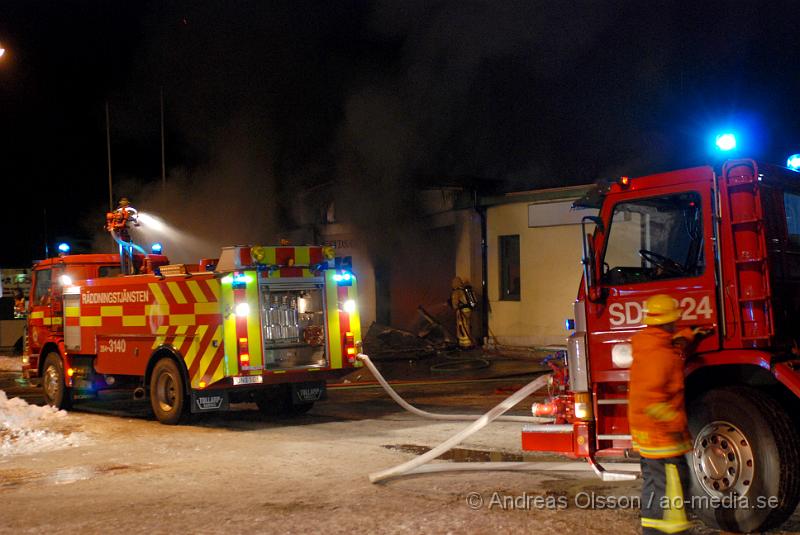 DSC_0095.JPG - Vid 01.30 larmades Räddningstjänsten från flera stationer samt ambulans och polis till Helsingborgsvägen i Ängelholm där man hade en fullt utvecklad brand i en byggnad som beräknas vara 30 meter bred och 100 meter lång, i byggnaden finns bland annat ett företag som sysslar med fyrverkerier och en bilverkstad. Så man vet inte om där finns gasolflaskor. En hel del fyrverkerier har smällt av. Man har ännu inte kontroll över branden då det även är svårt att få fram vatten eftersom brandposten har frusit fast. Ingen person ska ha skadats i branden.