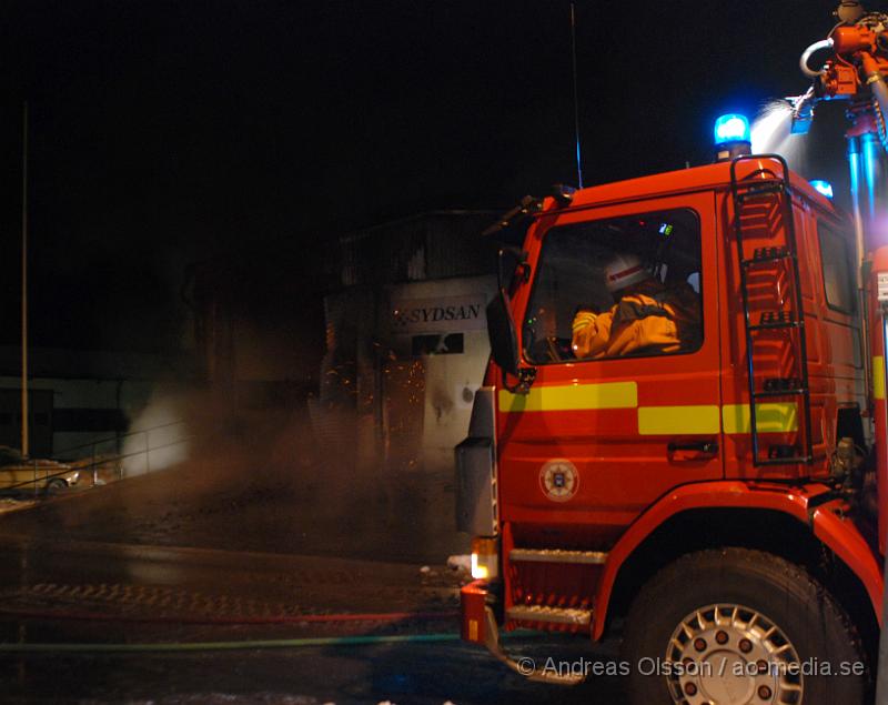 DSC_0099.JPG - Vid 01.30 larmades Räddningstjänsten från flera stationer samt ambulans och polis till Helsingborgsvägen i Ängelholm där man hade en fullt utvecklad brand i en byggnad som beräknas vara 30 meter bred och 100 meter lång, i byggnaden finns bland annat ett företag som sysslar med fyrverkerier och en bilverkstad. Så man vet inte om där finns gasolflaskor. En hel del fyrverkerier har smällt av. Man har ännu inte kontroll över branden då det även är svårt att få fram vatten eftersom brandposten har frusit fast. Ingen person ska ha skadats i branden.