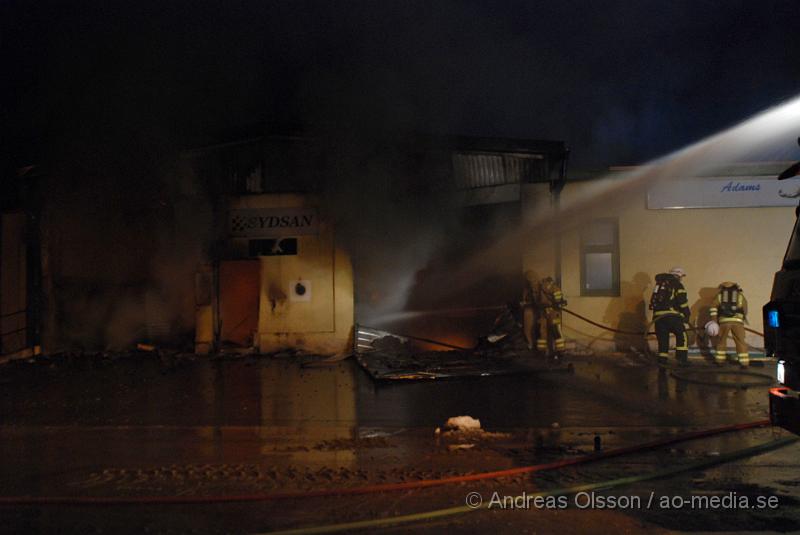 DSC_0101.JPG - Vid 01.30 larmades Räddningstjänsten från flera stationer samt ambulans och polis till Helsingborgsvägen i Ängelholm där man hade en fullt utvecklad brand i en byggnad som beräknas vara 30 meter bred och 100 meter lång, i byggnaden finns bland annat ett företag som sysslar med fyrverkerier och en bilverkstad. Så man vet inte om där finns gasolflaskor. En hel del fyrverkerier har smällt av. Man har ännu inte kontroll över branden då det även är svårt att få fram vatten eftersom brandposten har frusit fast. Ingen person ska ha skadats i branden.