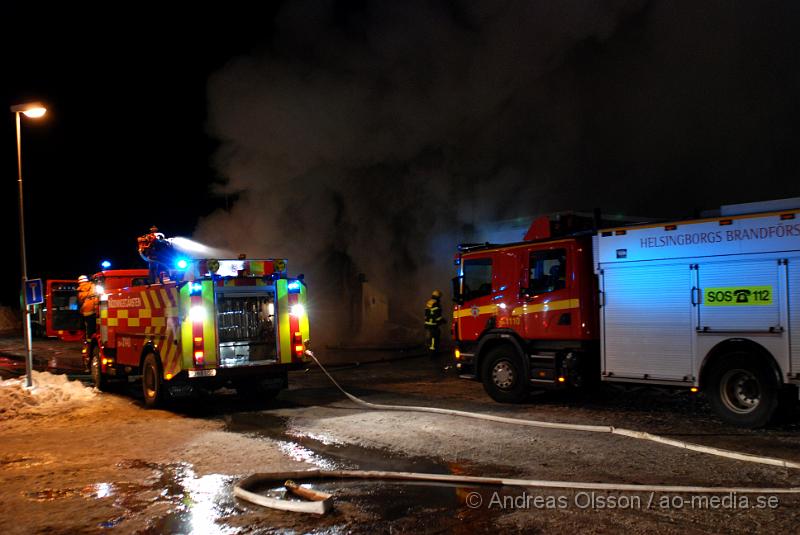 DSC_0108.JPG - Vid 01.30 larmades Räddningstjänsten från flera stationer samt ambulans och polis till Helsingborgsvägen i Ängelholm där man hade en fullt utvecklad brand i en byggnad som beräknas vara 30 meter bred och 100 meter lång, i byggnaden finns bland annat ett företag som sysslar med fyrverkerier och en bilverkstad. Så man vet inte om där finns gasolflaskor. En hel del fyrverkerier har smällt av. Man har ännu inte kontroll över branden då det även är svårt att få fram vatten eftersom brandposten har frusit fast. Ingen person ska ha skadats i branden.