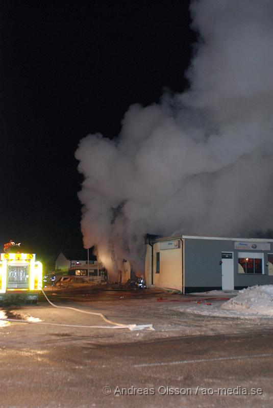 DSC_0127.JPG - Vid 01.30 larmades Räddningstjänsten från flera stationer samt ambulans och polis till Helsingborgsvägen i Ängelholm där man hade en fullt utvecklad brand i en byggnad som beräknas vara 30 meter bred och 100 meter lång, i byggnaden finns bland annat ett företag som sysslar med fyrverkerier och en bilverkstad. Så man vet inte om där finns gasolflaskor. En hel del fyrverkerier har smällt av. Man har ännu inte kontroll över branden då det även är svårt att få fram vatten eftersom brandposten har frusit fast. Ingen person ska ha skadats i branden.