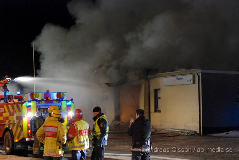 DSC_0168.JPG - Vid 01.30 larmades Räddningstjänsten från flera stationer samt ambulans och polis till Helsingborgsvägen i Ängelholm där man hade en fullt utvecklad brand i en byggnad som beräknas vara 30 meter bred och 100 meter lång, i byggnaden finns bland annat ett företag som sysslar med fyrverkerier och en bilverkstad. Så man vet inte om där finns gasolflaskor. En hel del fyrverkerier har smällt av. Man har ännu inte kontroll över branden då det även är svårt att få fram vatten eftersom brandposten har frusit fast. Ingen person ska ha skadats i branden.